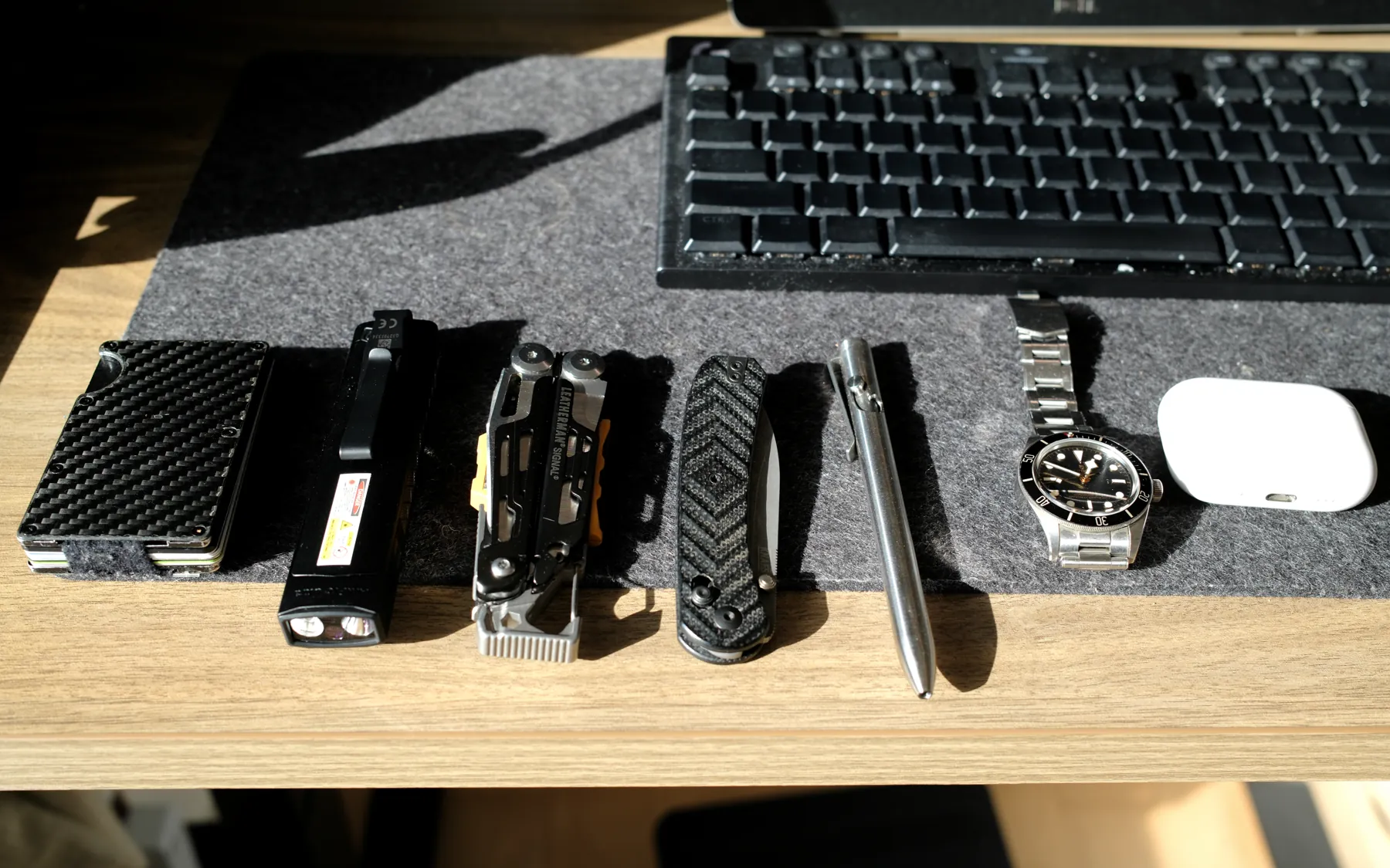 Wallet, flashlight, multi-tool, knife, pen, watch and earbuds lined up on the mat